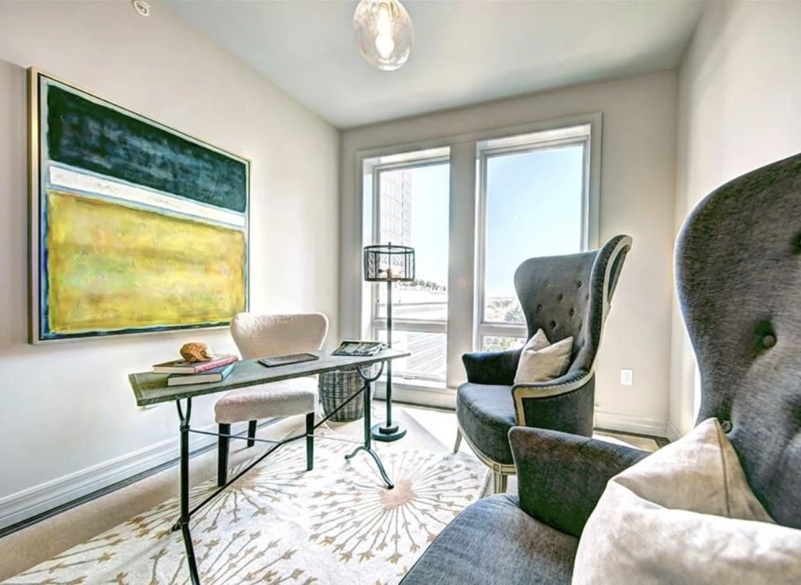 Light-filled sitting room with sculptural chairs, a glass desk, and colorful artwork